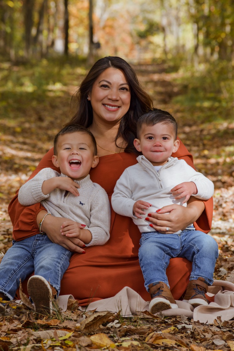 A mother smiling with her two young children outdoors